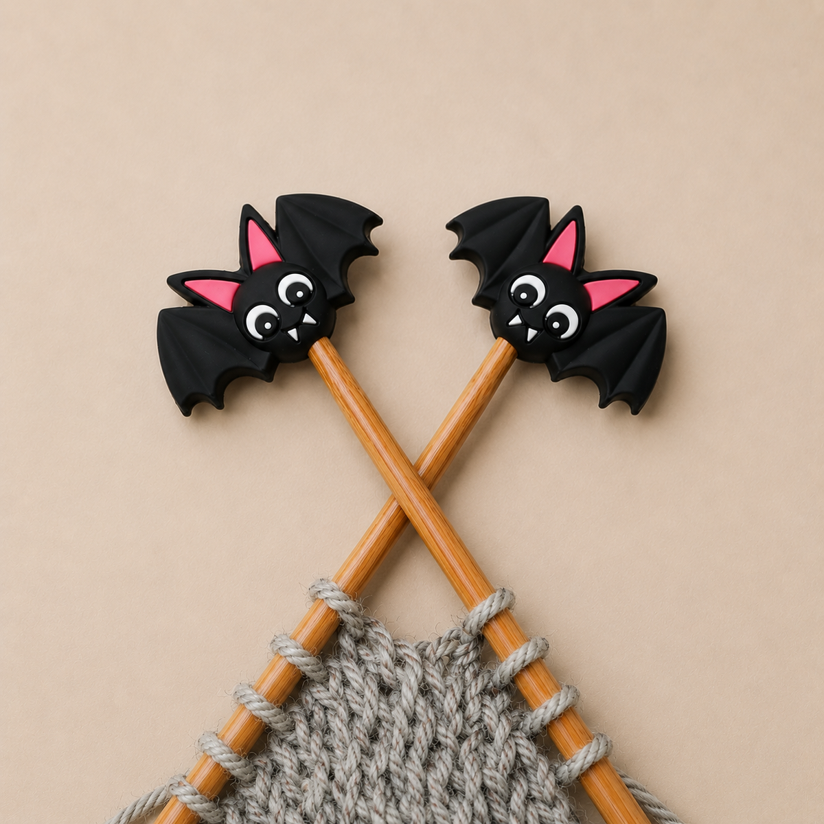 Overhead view of black Bat silicone stitch stoppers on crossed wooden needle tips holding grey knitting