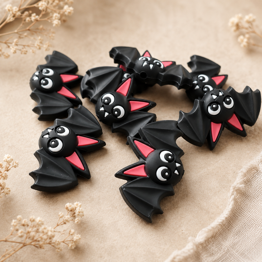 Black Bat silicone stitch stoppers with outstretched wings, pink ears and white fangs arranged on a beige surface